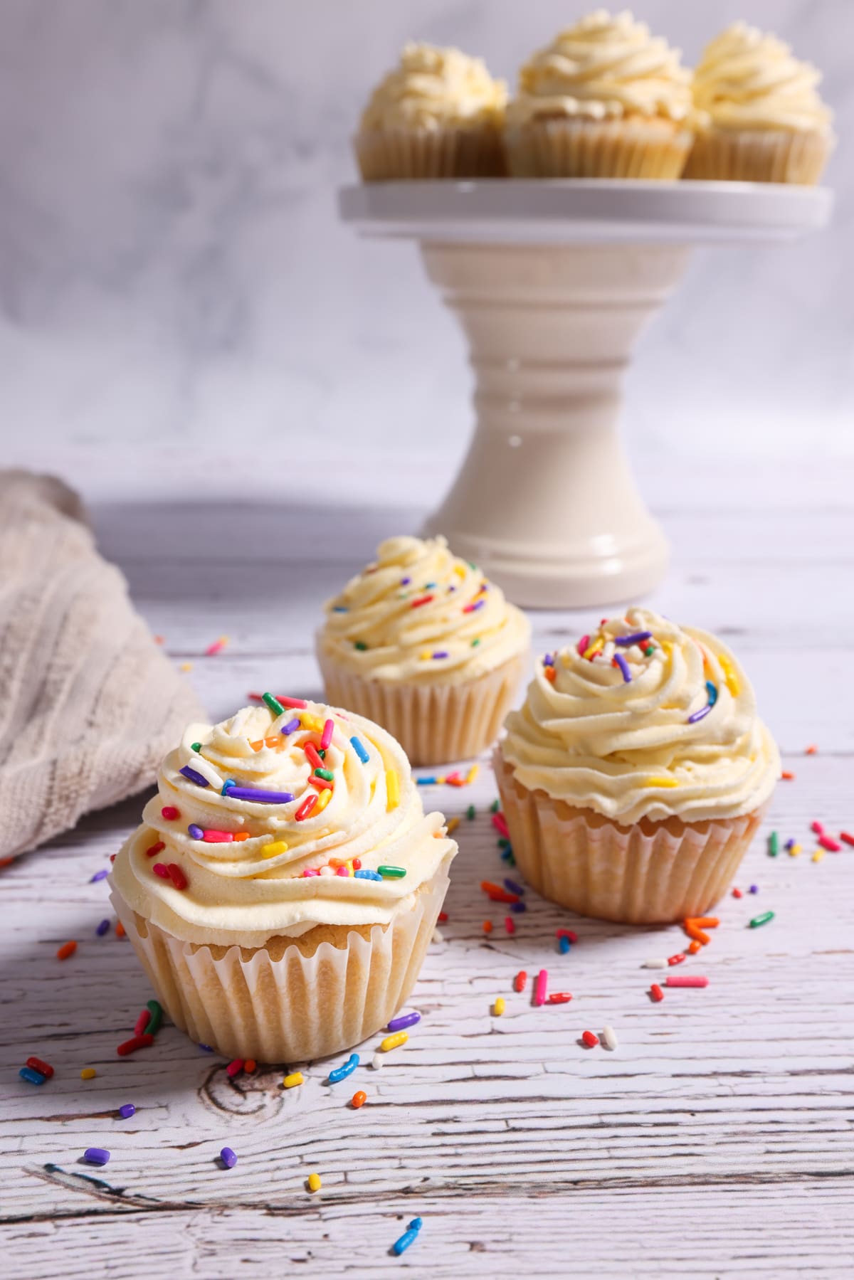 Three sourdough discard cupcakes on a table with sprinkles and vanilla buttercream frosting